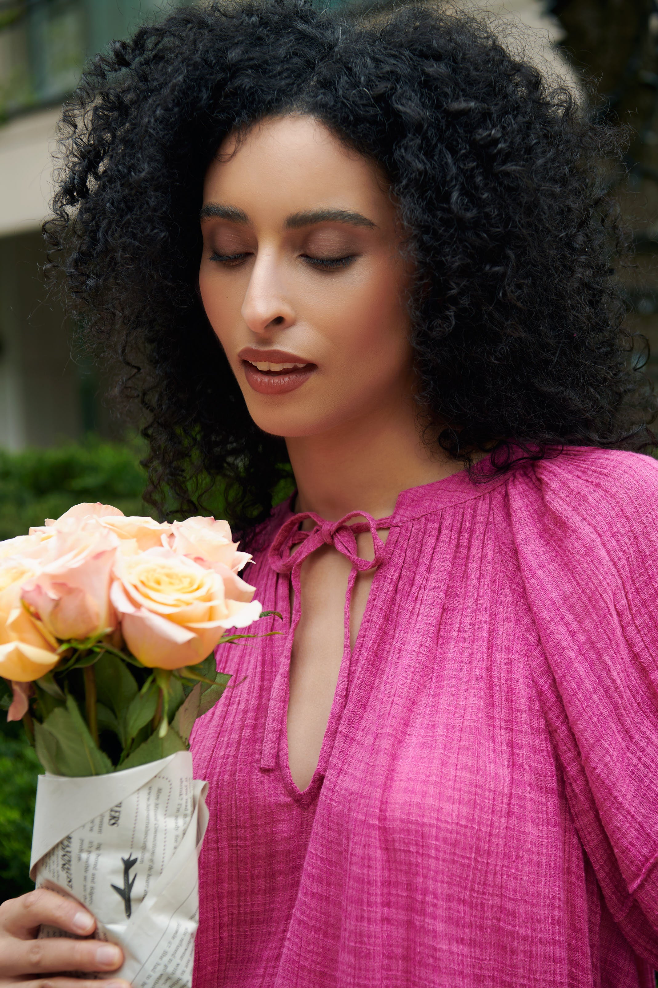 A woman smells fresh flowers wrapped in newspaper while wearing The Lumina Popover Top by Apiece Apart 