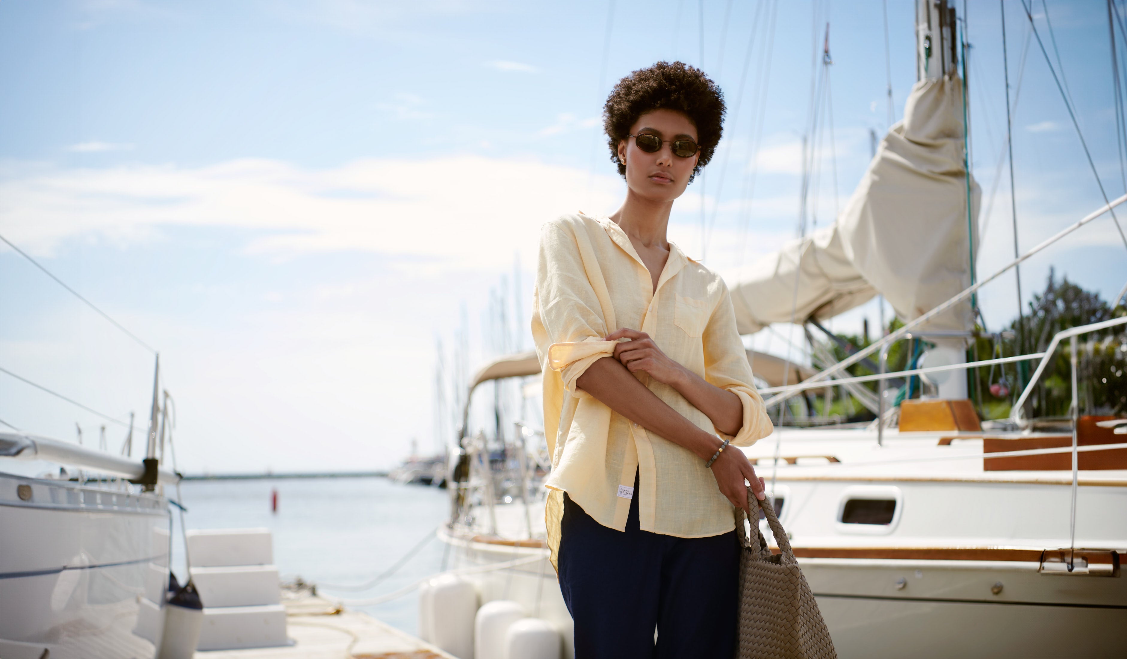 Woman stands on a dock beside a yacht wearing Frank & Eileen's relaxed button up shirt and linen pant