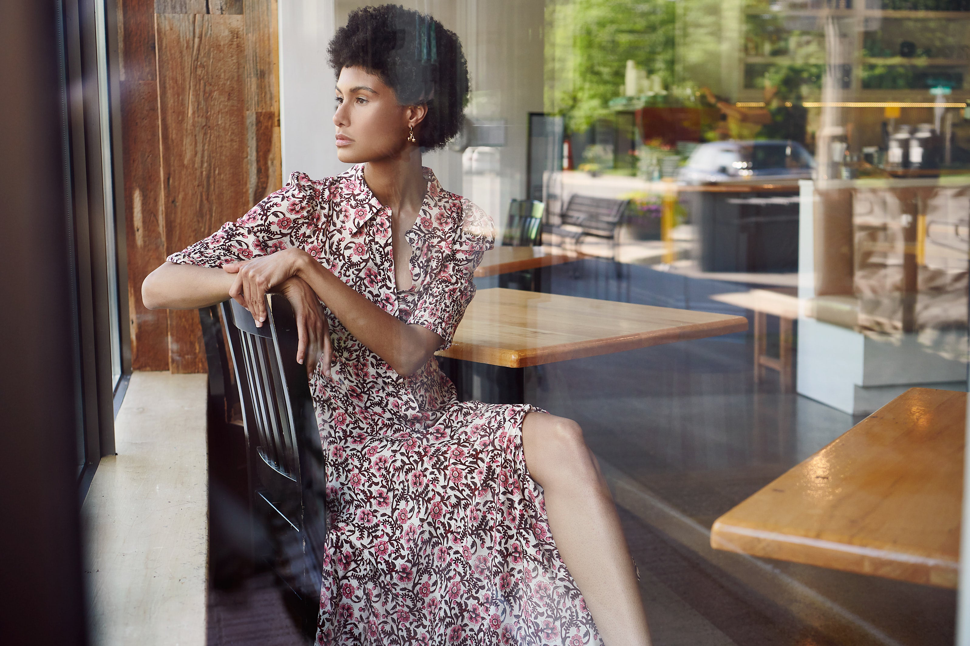 A woman wearing the Bloom Print Midi Dress by RIXO looks out a window